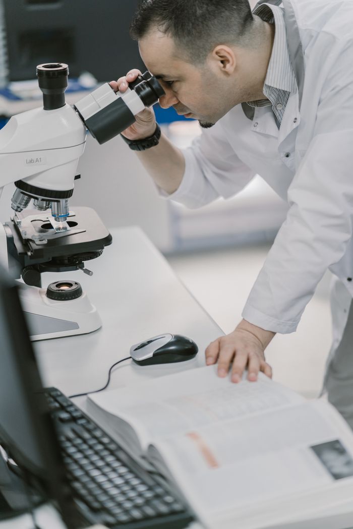 hero-img-01 Scientist in a lab coat examines samples using a microscope. Professional laboratory environment.